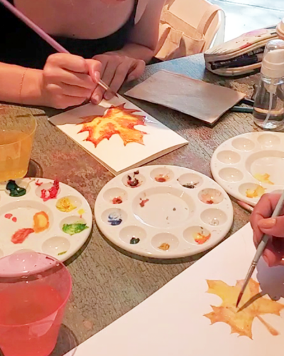 Two people painting fall maple leaves with watercolors during a LaLaLu workshop